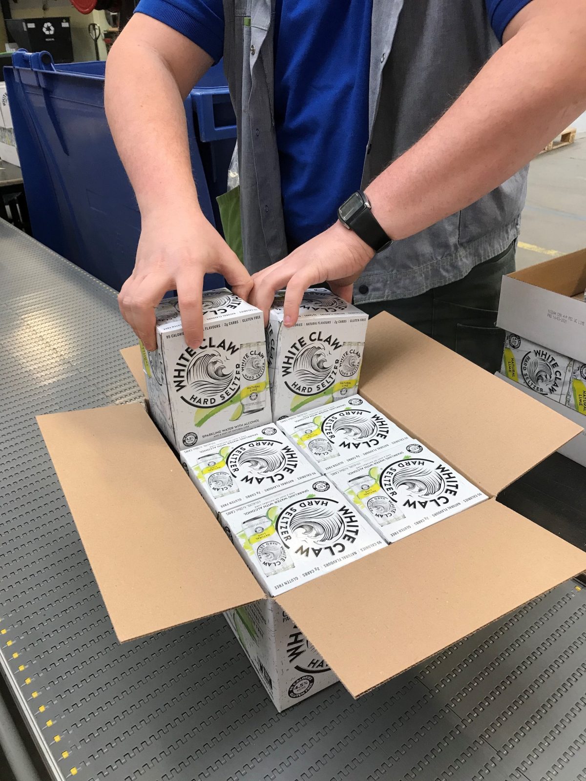 Een een kartonen doos passen 6 aparte verpakkingen met daarin blikjes. Een medewerker van Bewel vult de dozen.