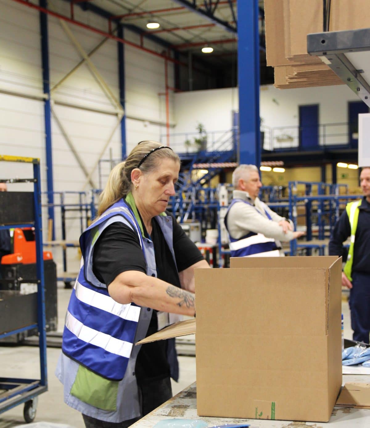 Een medewerker van Bewel is bezig met producten te verpakken in een grotere kartonnen doos, die op een werktafel staat.